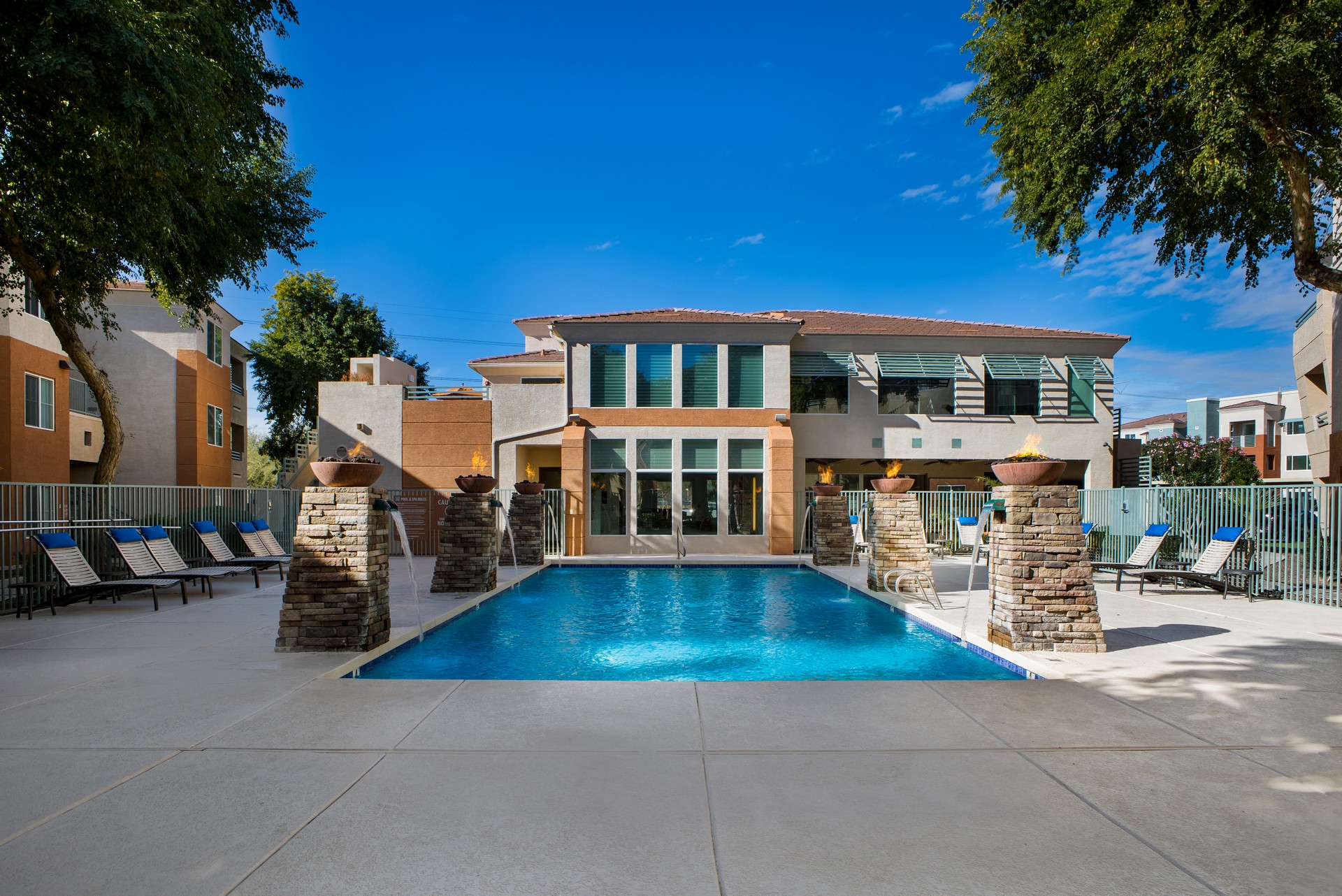 a swimming pool in front of a house with a patio and chairs