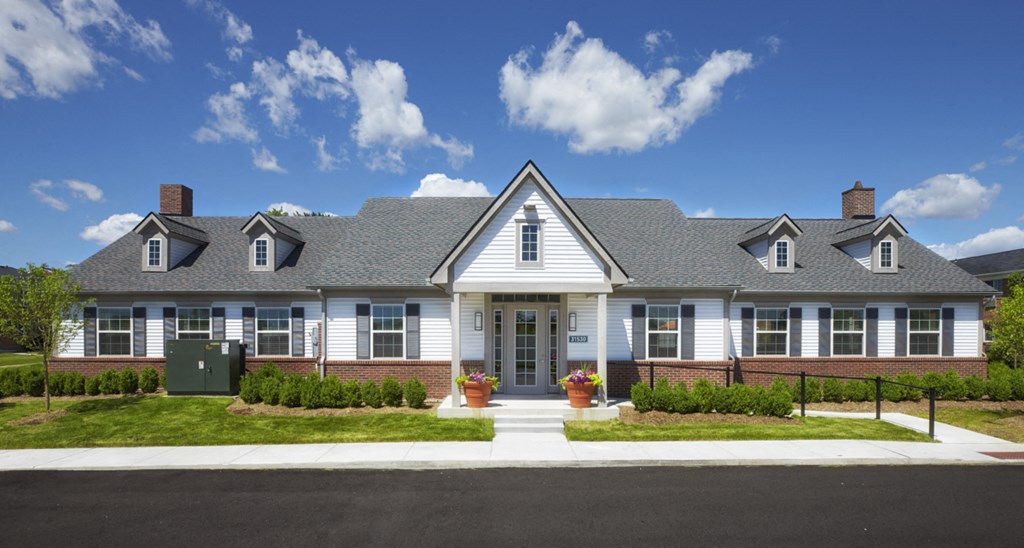 A white house with a grey roof and a green trash can in front.