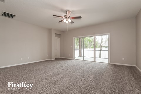 A spacious room with a ceiling fan and sliding glass doors leading to a balcony.
