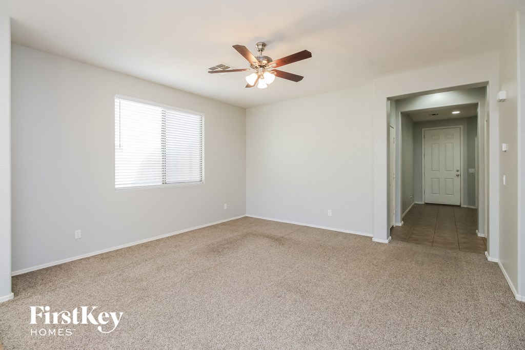 an empty living room with a ceiling fan and a door to a hallway