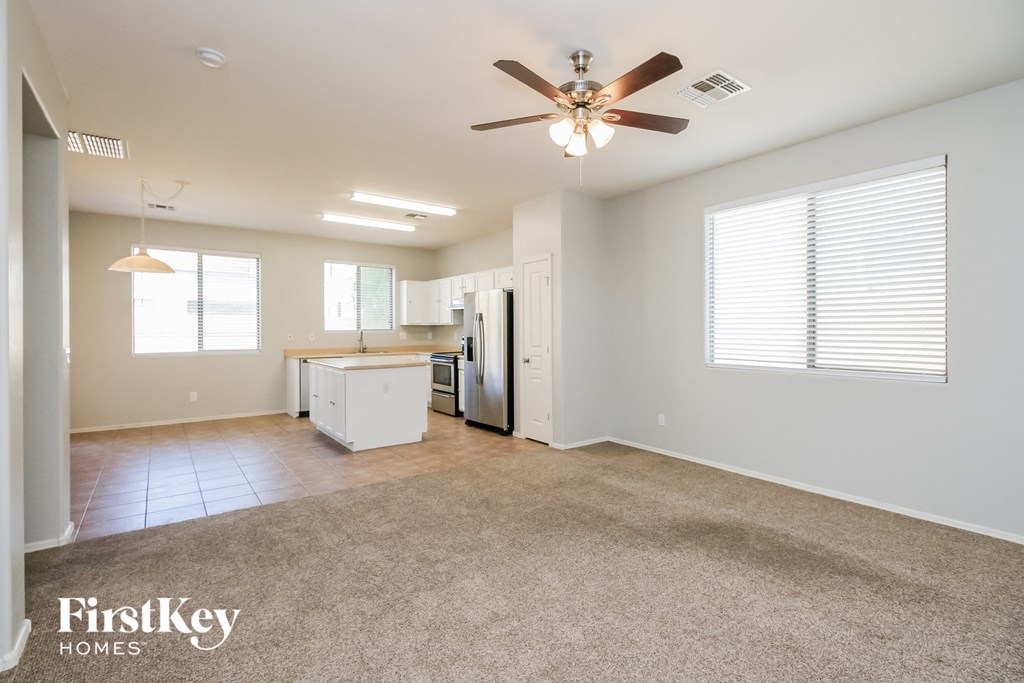 an empty living room with a ceiling fan and a kitchen