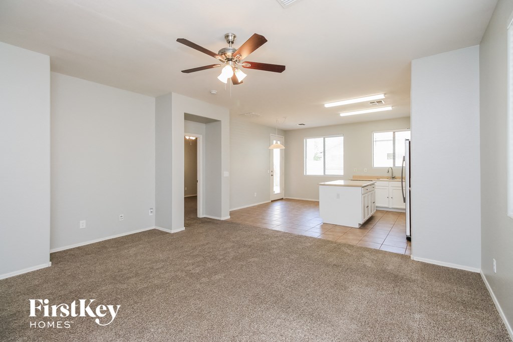an empty living room with a ceiling fan and a kitchen