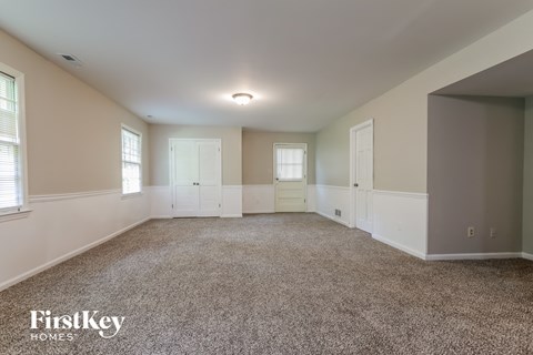 A spacious room with a carpeted floor and white walls, with a FirstKey Homes logo in the corner.