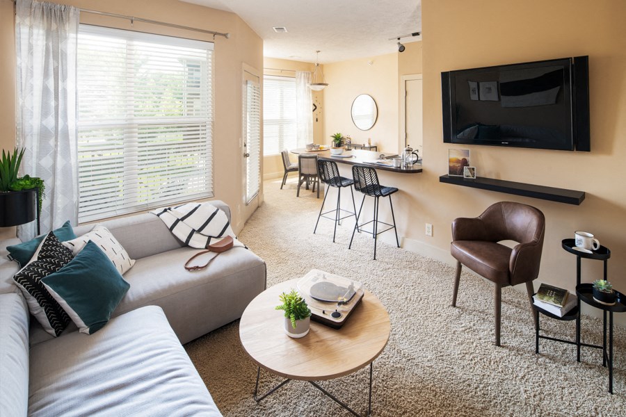 A living room with a white couch, a brown leather chair, and a flat screen TV mounted on the wall.