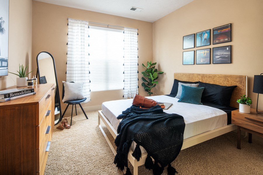 A bedroom with a bed, chair, and a plant.