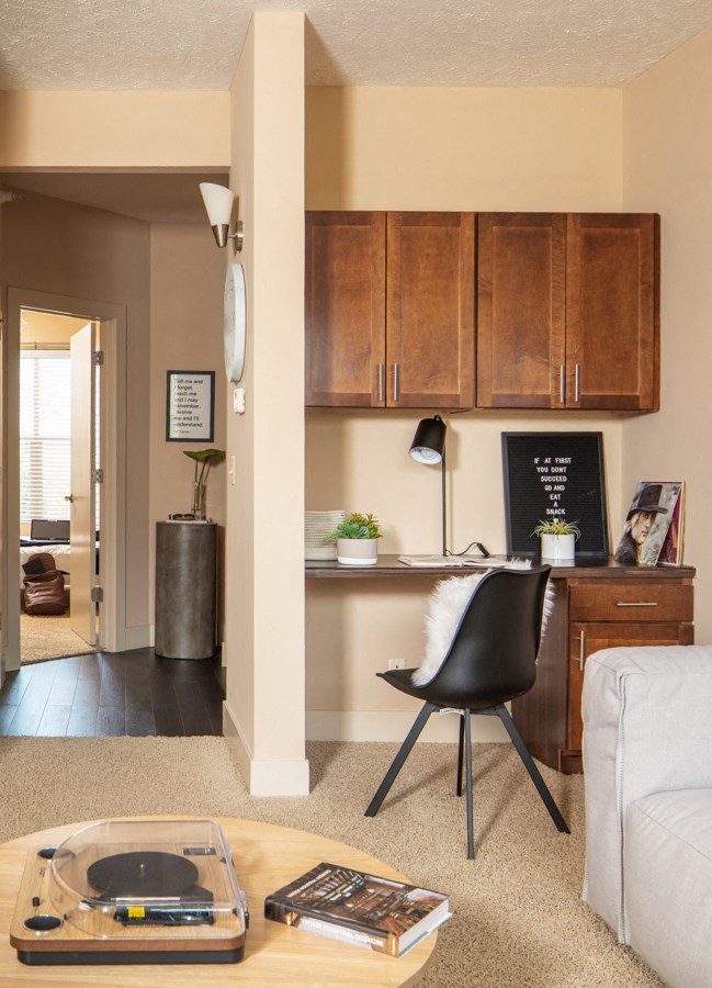 A black chair sits in front of a desk with a laptop and a plant on it.