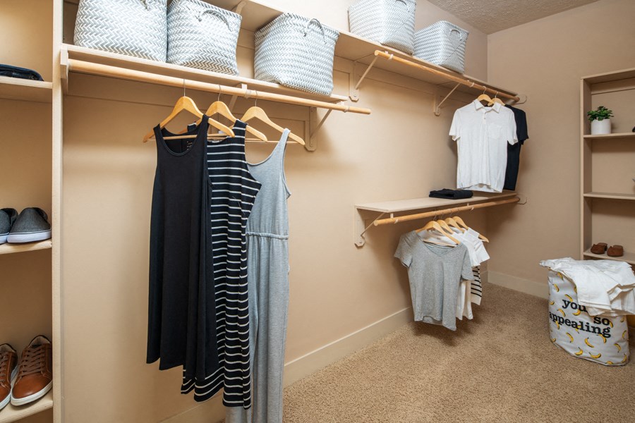 A closet with clothes and shoes on shelves and hangers.