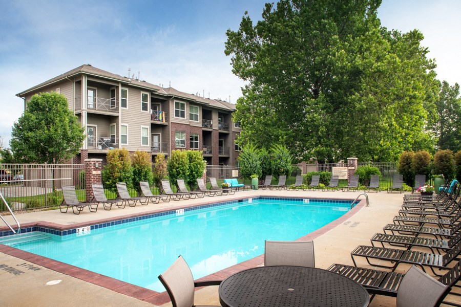 A large swimming pool surrounded by lounge chairs and apartment buildings.