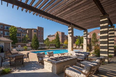 A patio with a pool and chairs under a wooden roof.