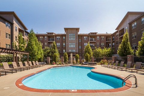 a swimming pool with chairs around it in front of an apartment building