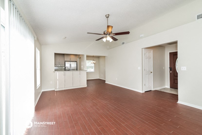 an empty living room with a ceiling fan and a kitchen