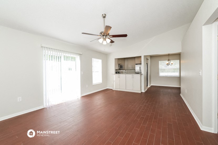 an empty living room with a ceiling fan and a kitchen
