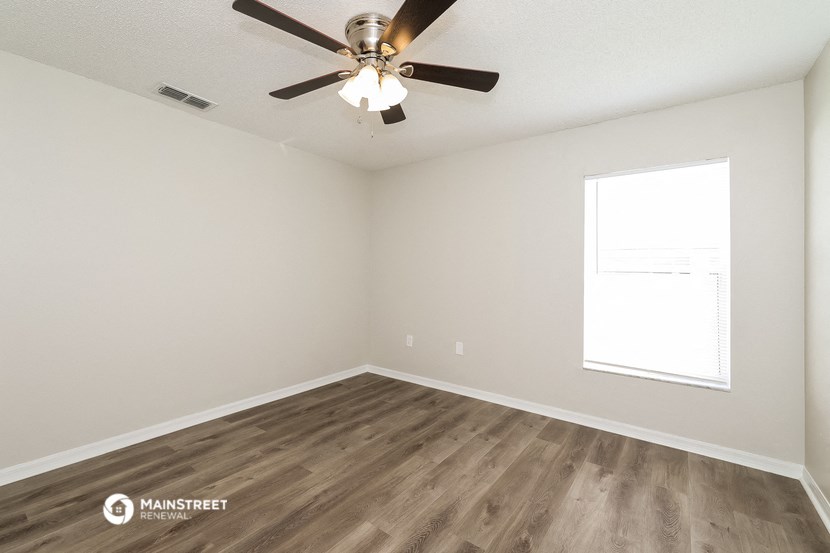 the spacious living room with wood flooring and a ceiling fan