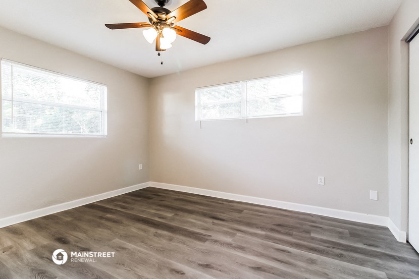 an empty living room with a ceiling fan and two windows