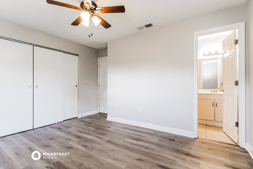 the spacious living room with a ceiling fan and white walls