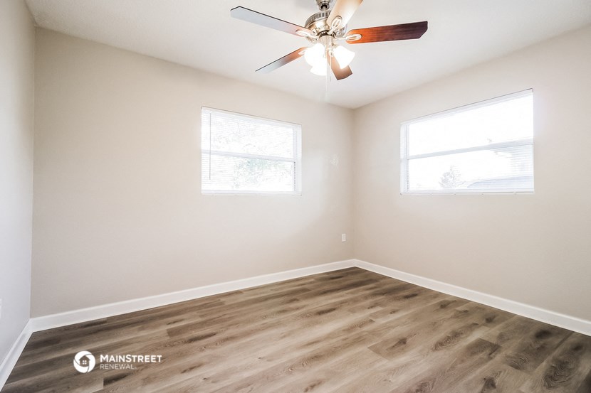 an empty room with a ceiling fan and two windows