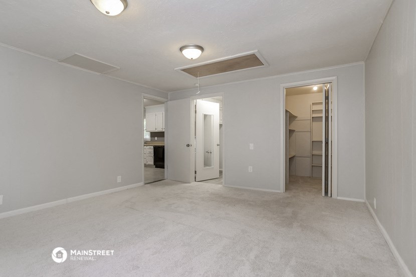 an empty living room with a hallway to the kitchen and a closet