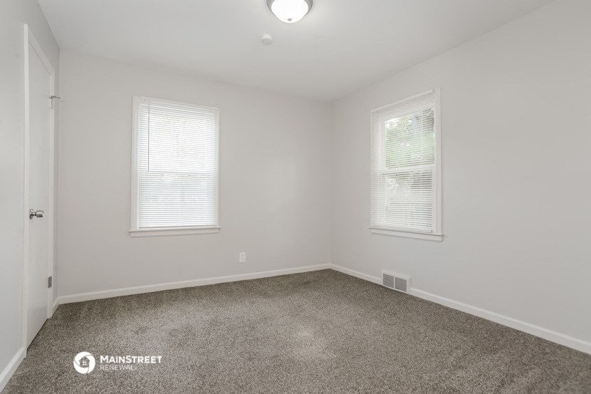 a spacious room with carpet and two windows