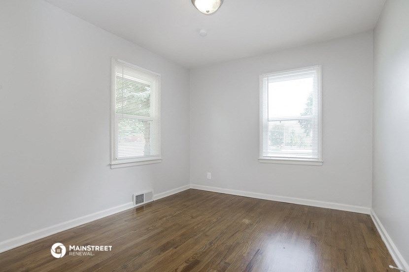 a bedroom with white walls and wood flooring and two windows
