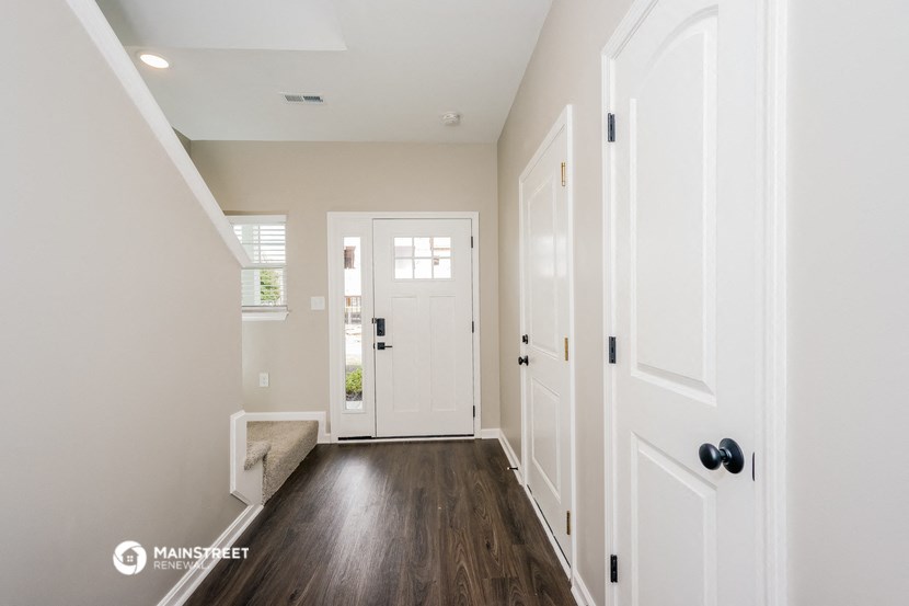 the hallway of a home with white walls and wooden floors and a white door