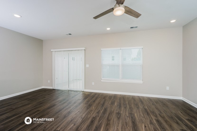 the spacious living room with wood flooring and a ceiling fan
