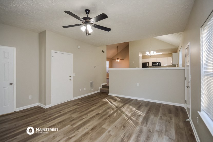 an empty living room with a ceiling fan and a kitchen