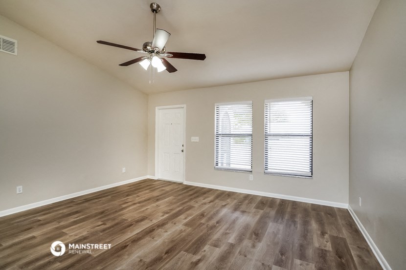 the spacious living room with wood flooring and a ceiling fan