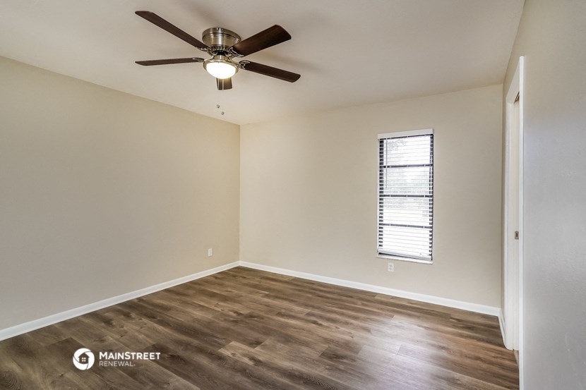 the spacious living room with wood flooring and a ceiling fan