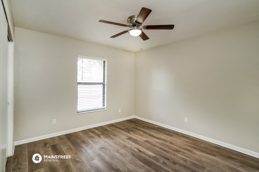 the spacious living room with wood flooring and a ceiling fan