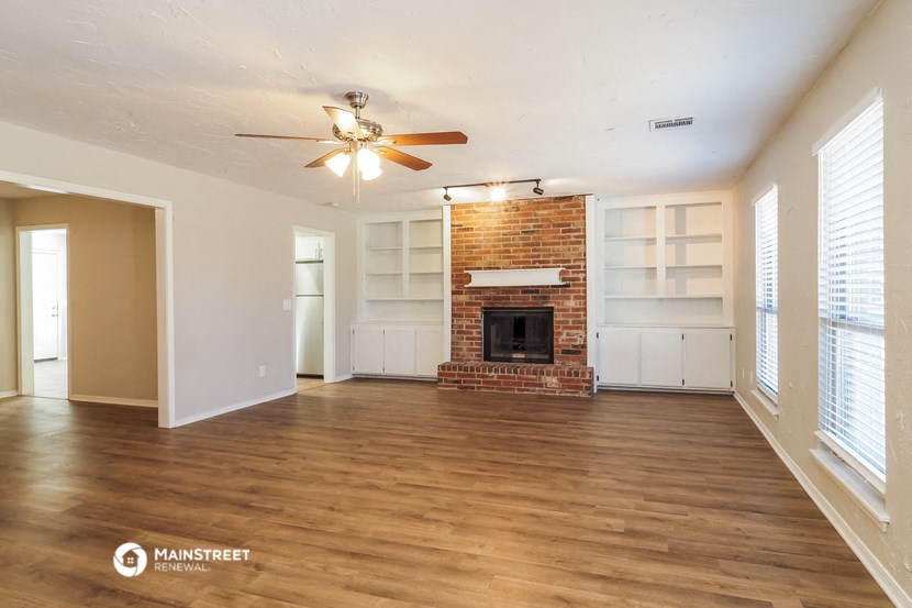 an empty living room with a brick fireplace and a ceiling fan