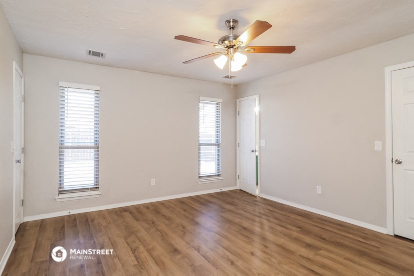 the spacious living room with hardwood flooring and a ceiling fan