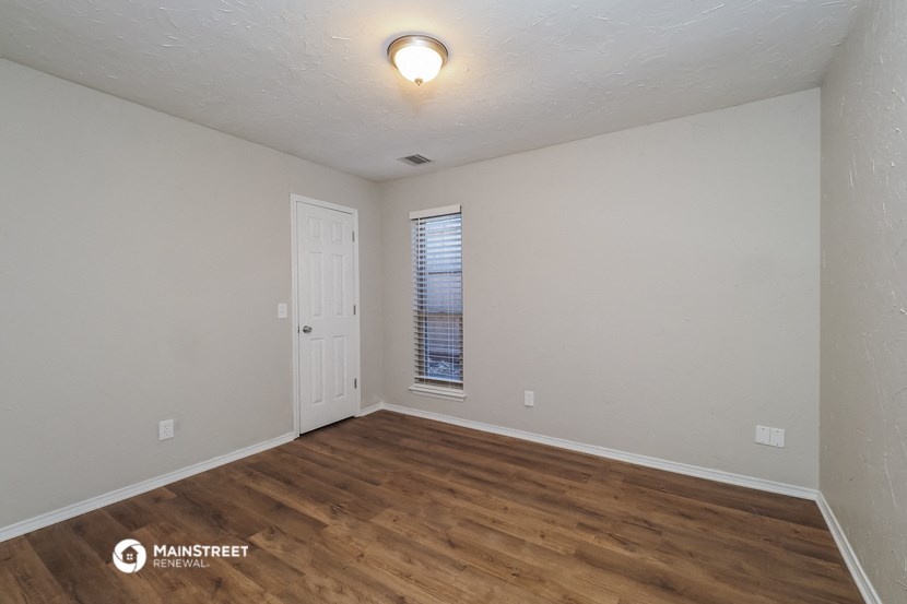 the living room of an apartment with wood flooring and white walls