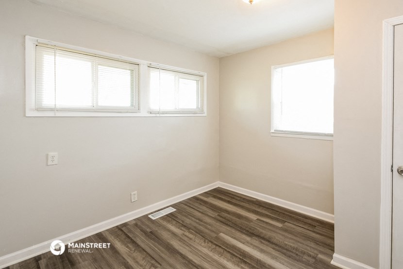 the interior of an empty room with wood flooring and two windows