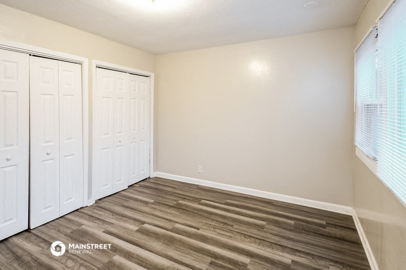 the interior of a bedroom with three closets and wood flooring