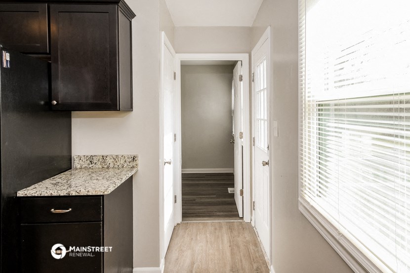a hallway with a large window and a kitchen with wood floors and a black cabinet