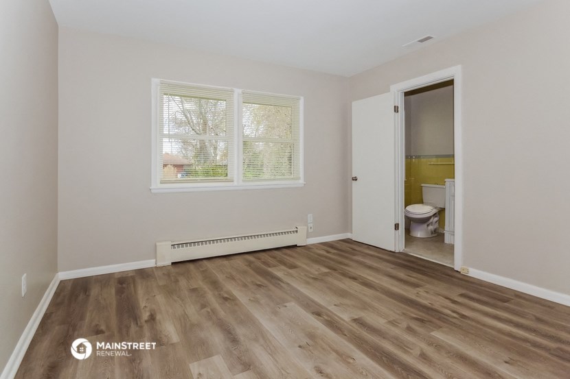 the living room of a home with a wooden floor and a door to a bathroom