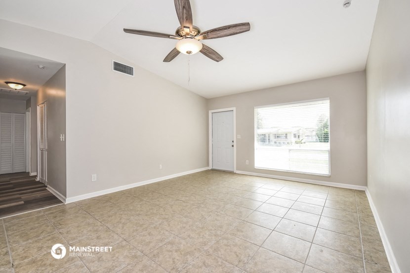 an empty living room with a ceiling fan and tiled floor