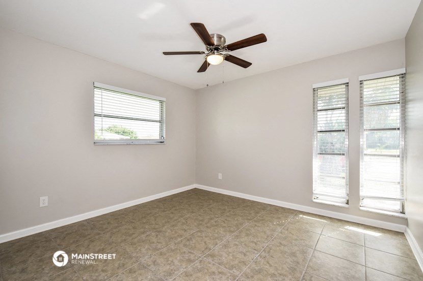 an empty room with a ceiling fan and two windows
