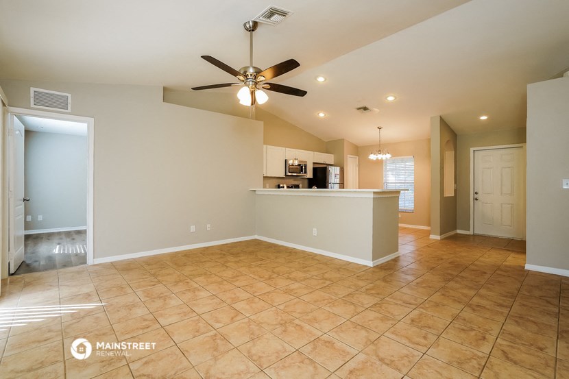 an empty living room with a kitchen and a ceiling fan
