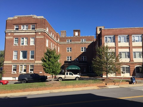 A red car is parked on the side of the road in front of a brick building.