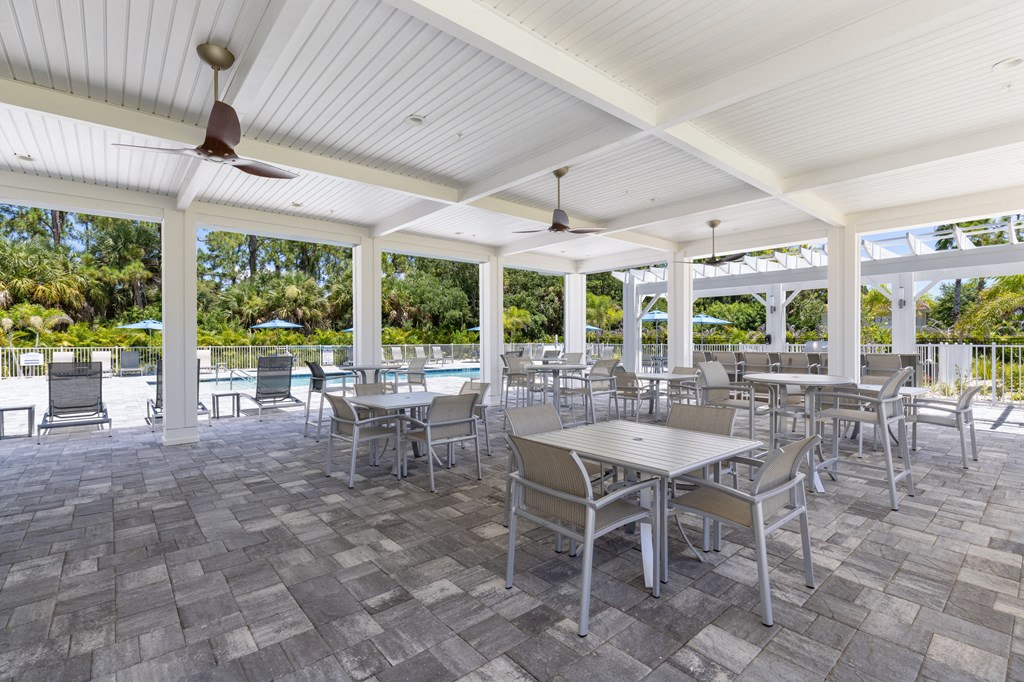 a patio with tables and chairs and a pool in the background