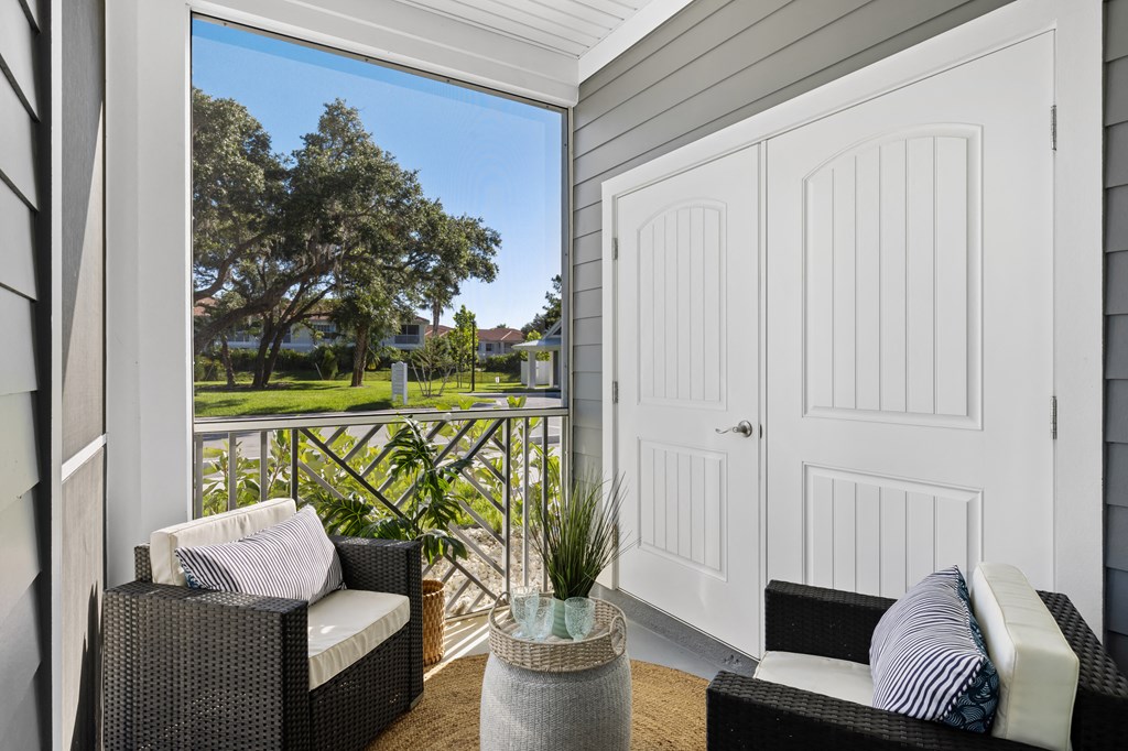 a porch with two chairs and a white door and a view of a golf course