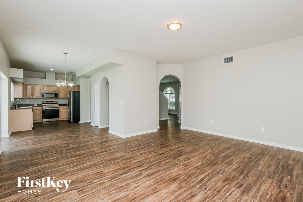 an empty living room with wood flooring and a kitchen