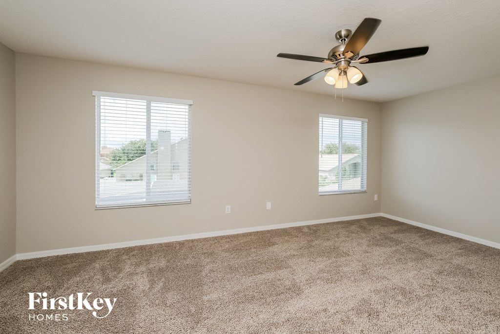 an empty living room with a ceiling fan and two windows