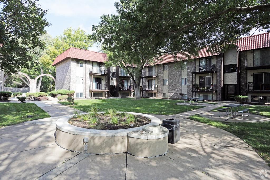 a courtyard with benches and trees in front of an apartment building