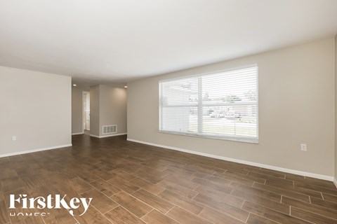 A spacious room with wooden flooring and a large window with blinds.