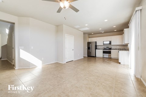 A spacious kitchen and living room with a ceiling fan and beige tiled floors.