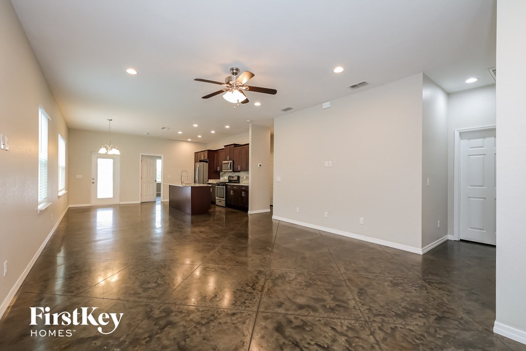 A spacious room with a ceiling fan and a kitchen area in the background.