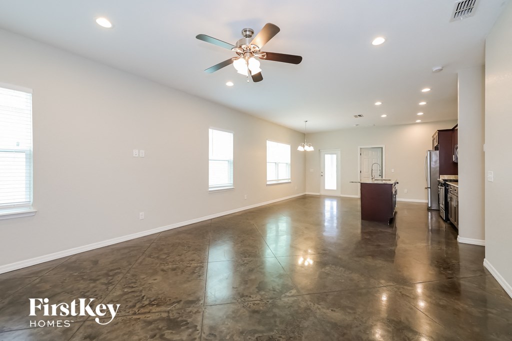 A spacious room with a ceiling fan and a kitchen area in the background.