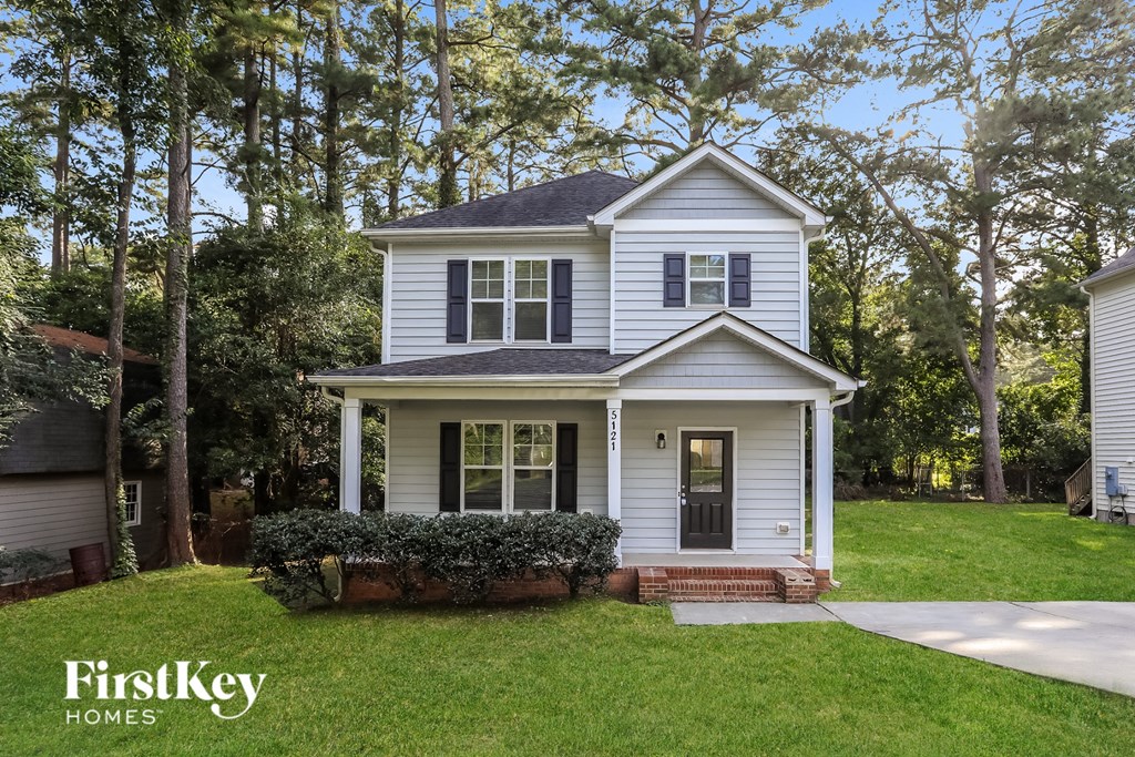 A white house with a black door and windows is surrounded by greenery.